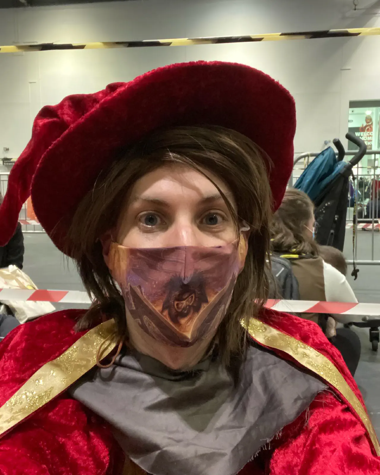 A selfie of myself, sitting down in a red wizards hat and robes, in cosplay as Rincewind