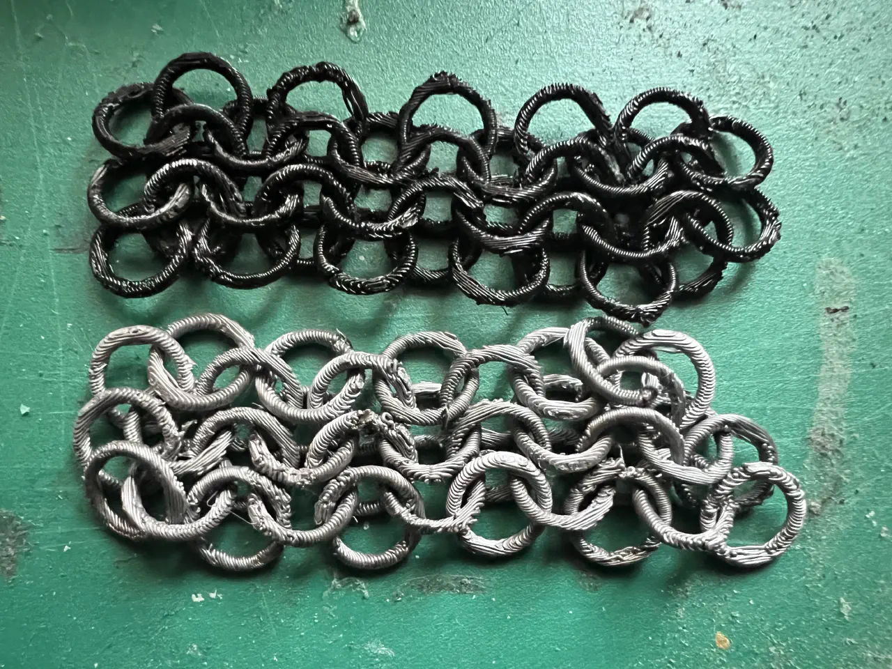 Two small sections of chainmail, one in black and one in silver side by side