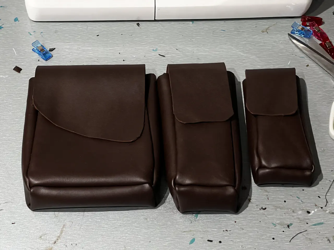 One thick and two thin pouches made of brown faux leather next to each other on a table.