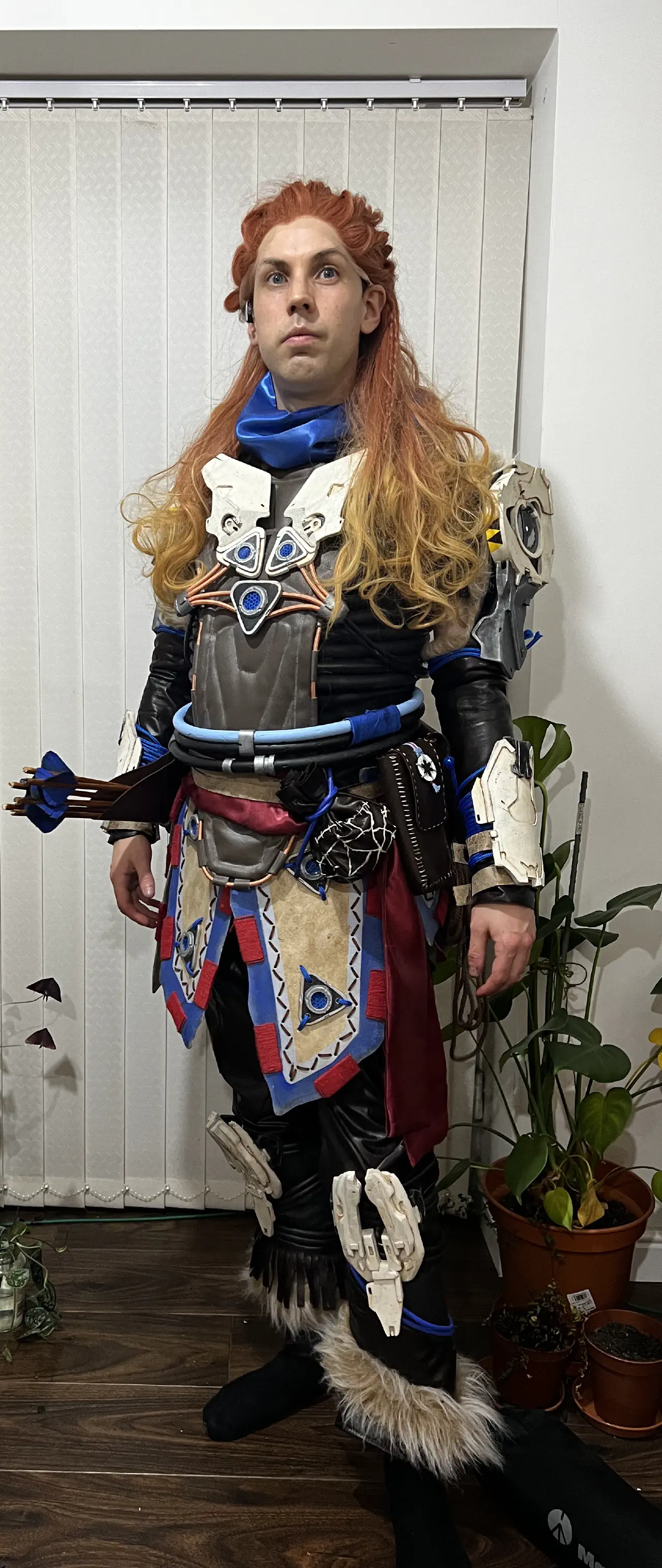 A person standing in front of blinds dressed as Aloy in the Shield Weaver outfit.