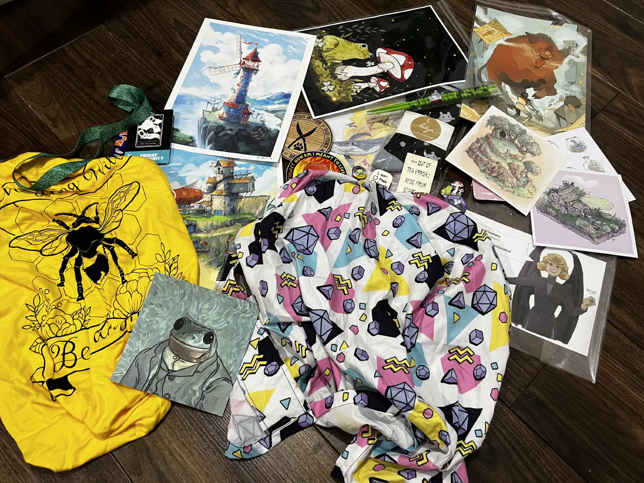 A collection of art prints, badges and clothing laid on a wooden floor.