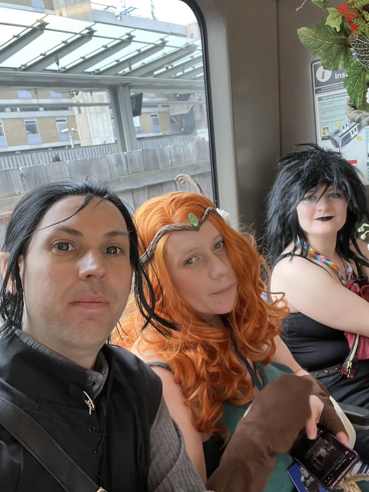 Three people, one dressed as Vax, one as Keyleth and one as Death from Sandman looking at the camera whilst sat on a train.