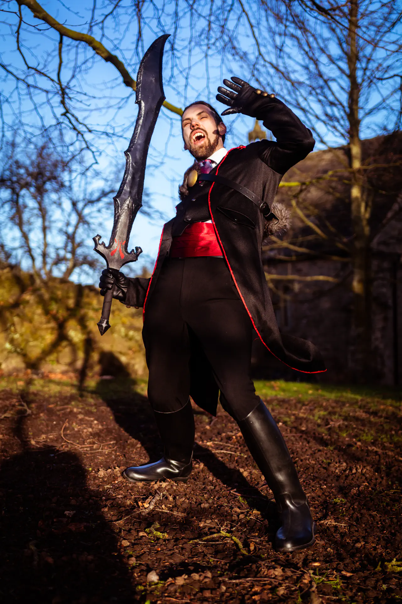 An bearded individual dressed in a black tailcoat accentuated by red accessories and wielding a black sword is recoiling from the sunlight