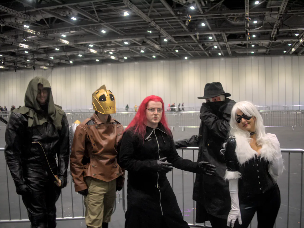 Four individuals dressed in cosplay in a plain, open hall. From left to right are the green arrow, rocketeer, axel from kingdom hearts, darkman and black cat