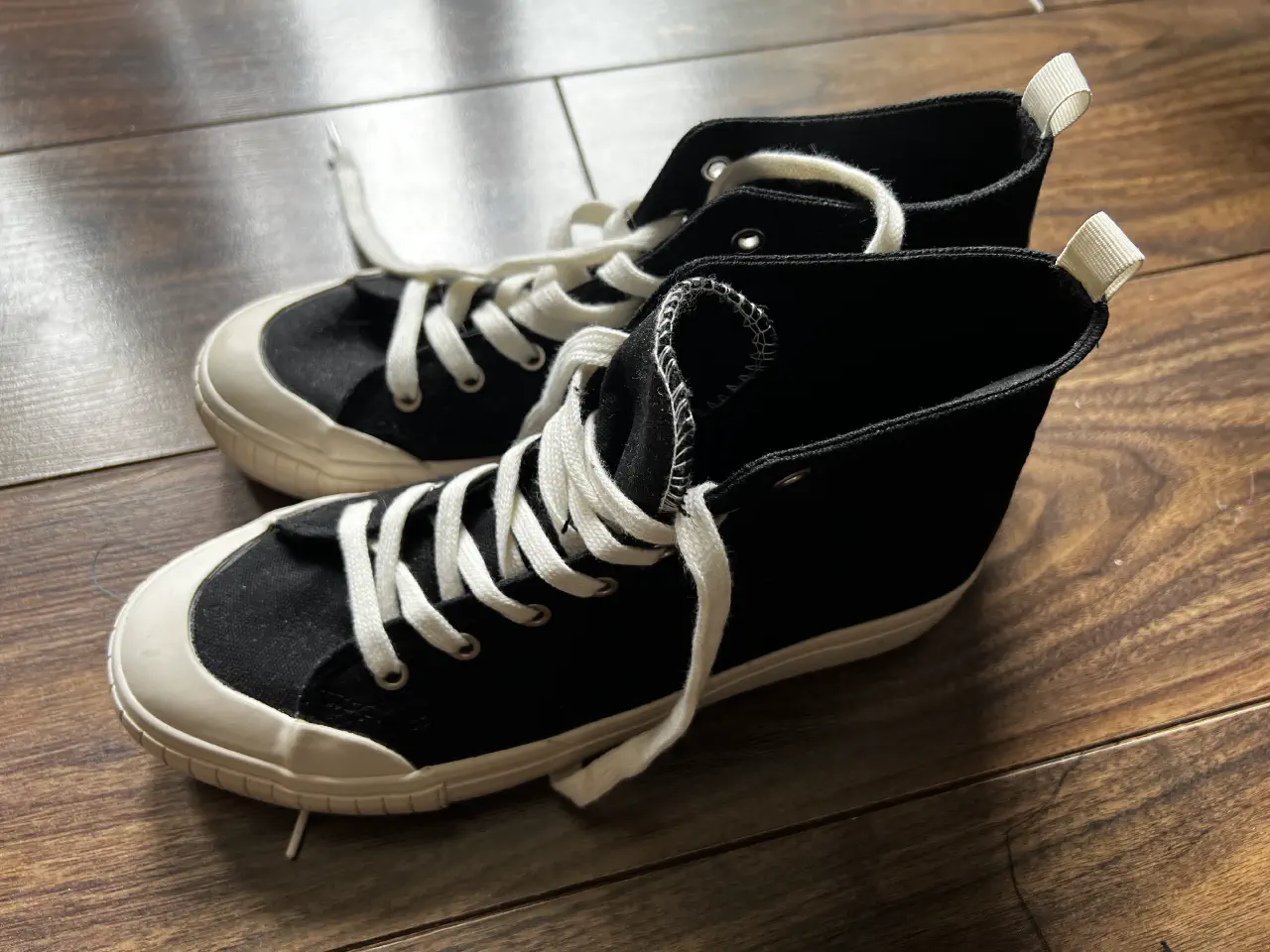 A pair of black and white canvas ankle high shoes on a wooden floor.